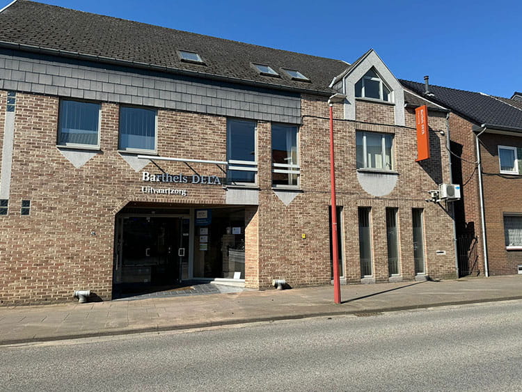Aanzicht buitengevel met lichte baksteen en roestbruine pilaar waarop Uitvaartzorg Barthels DELA staat